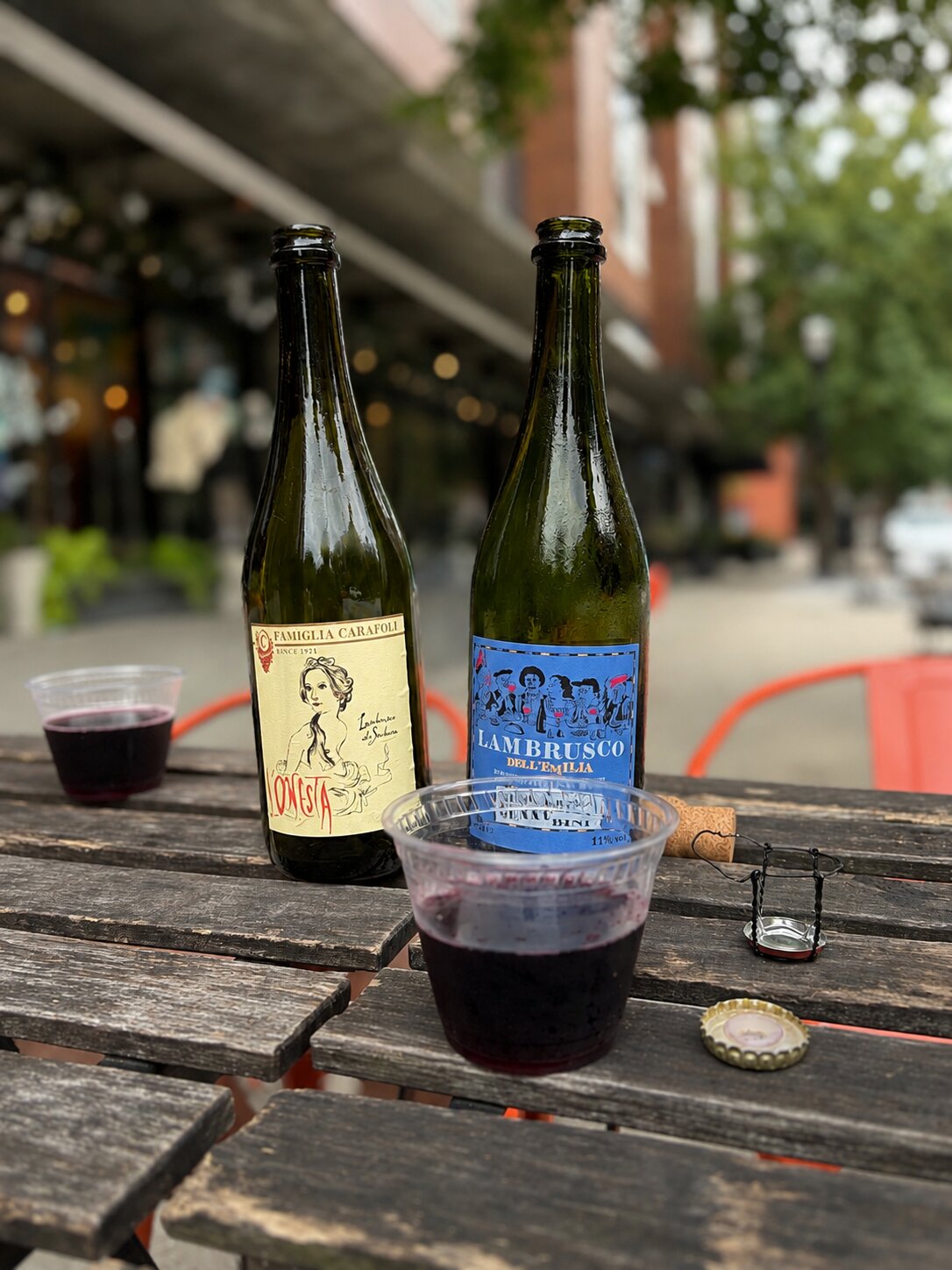 Two bottles of chilled Lambrusco and filled glasses on a wooden outdoor table
